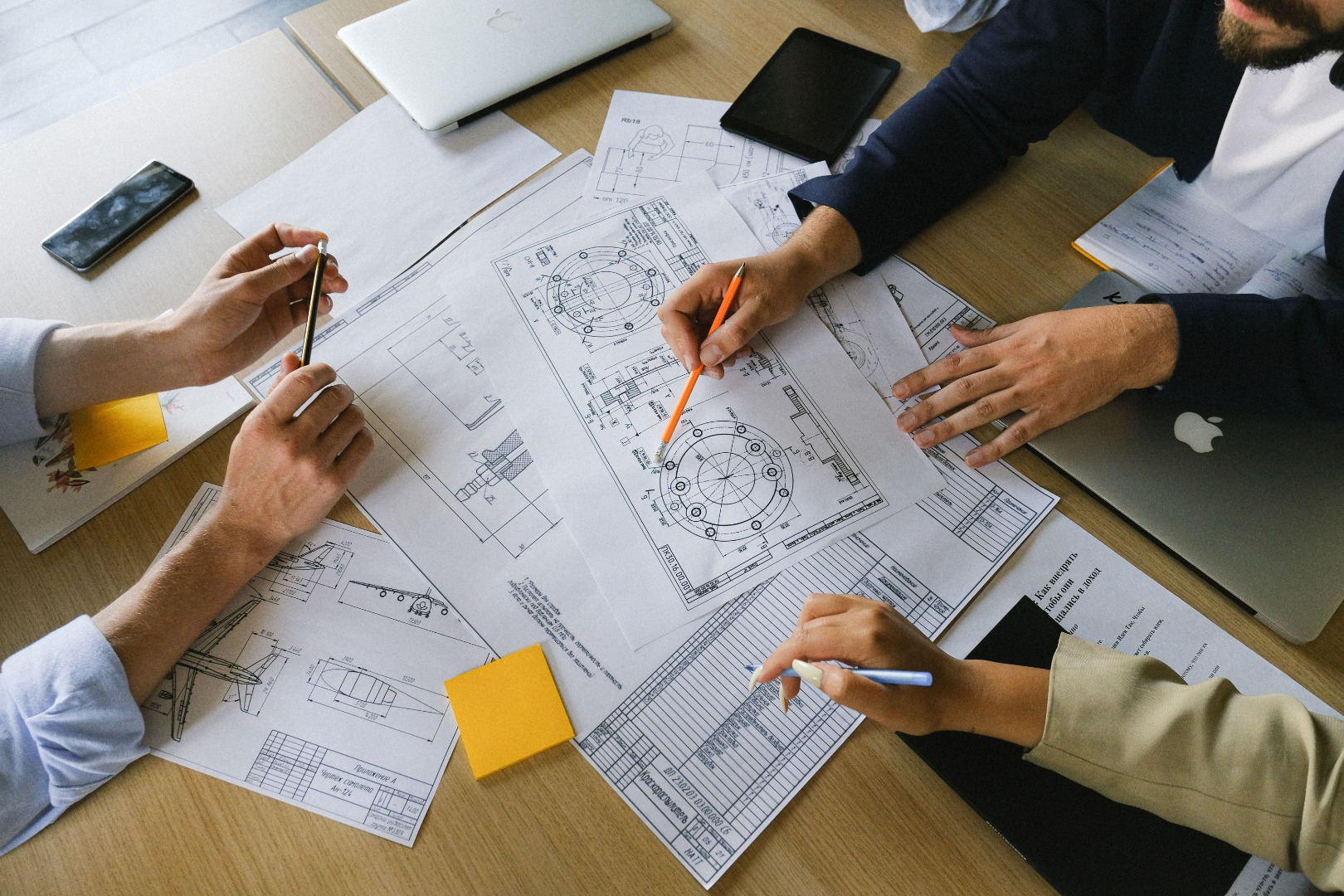 Engineers reviewing mechanical drawings and tolerance callouts around a table